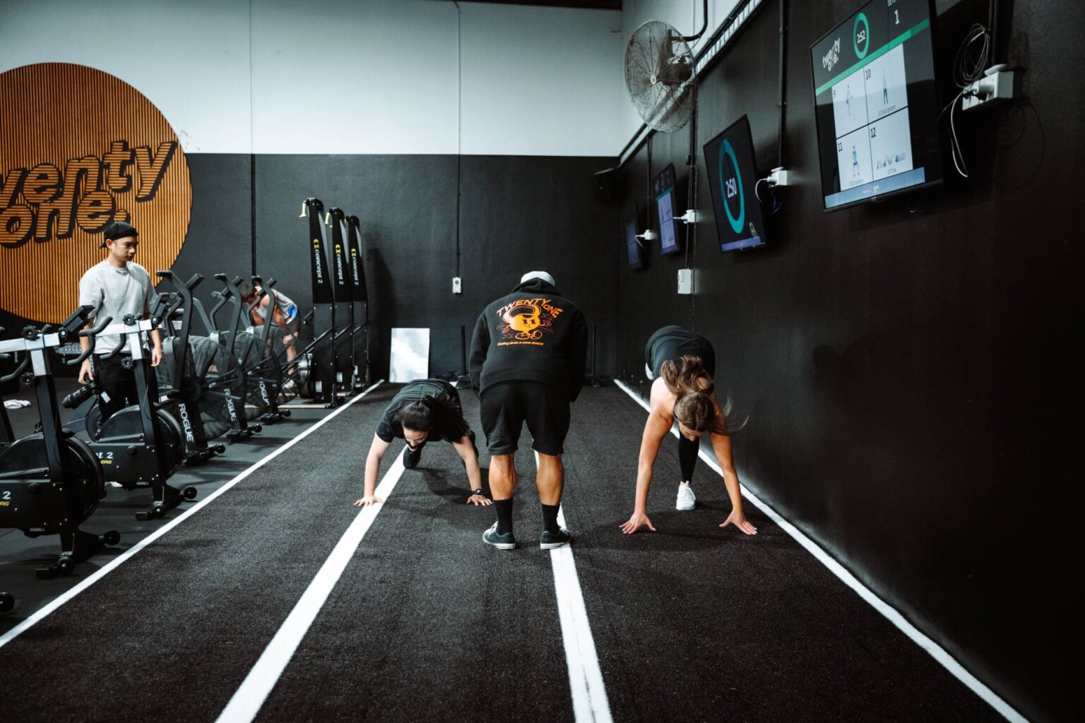 Personal trainer encouraging two women doing burpees on astroturf at Twenty One Training gym in airport west